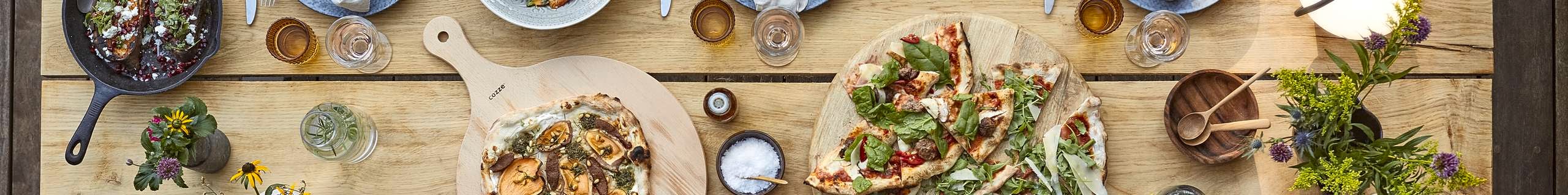 Birds-eye view of dining table set for six people, with two pizzas and various plates of food placed throughout.