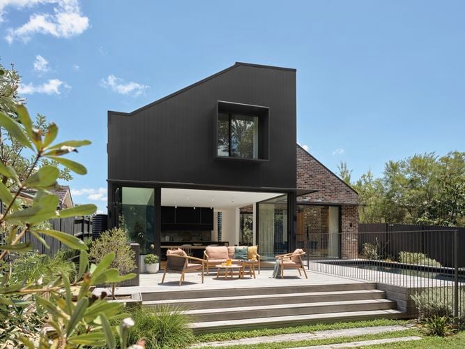 Modern dark colours home opening out to outdoor entertaining area with timber setting and steps down to lawn