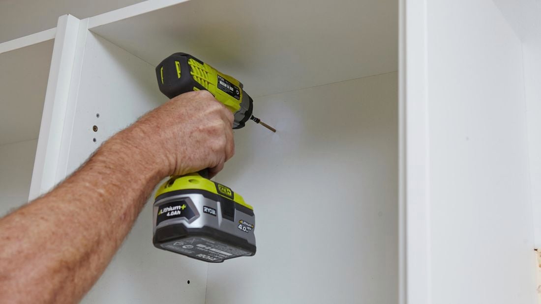 A screw being drilled into the back of a kitchen wall cabinet