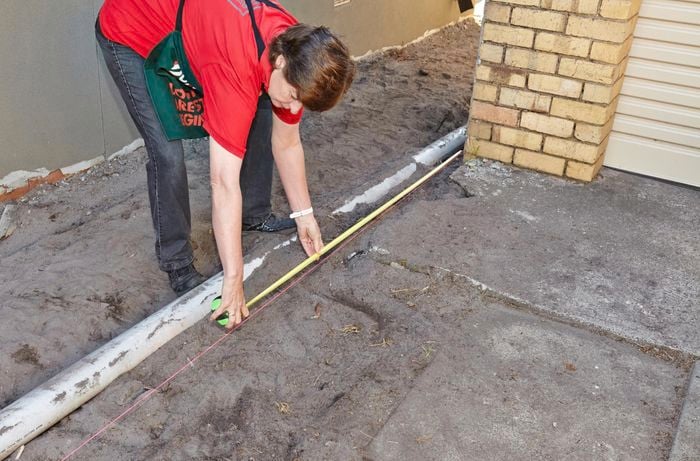 A Bunnings team member marking out the position of a posthole using string and a tape measure