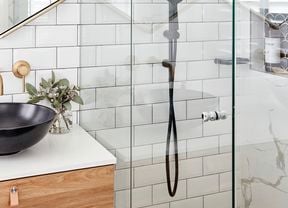 Glass shower with white tiled walls and black sink on timber cabinet