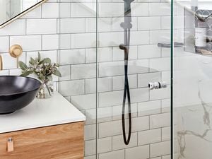 Glass shower with white tiled walls and black sink on timber cabinet