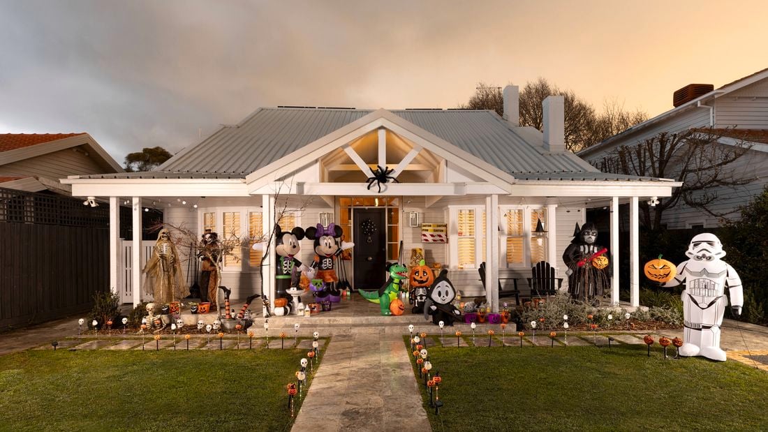 A white house decorated for Halloween with inflatables, pumpkins, skeletons, and themed figures on the porch and front yard.