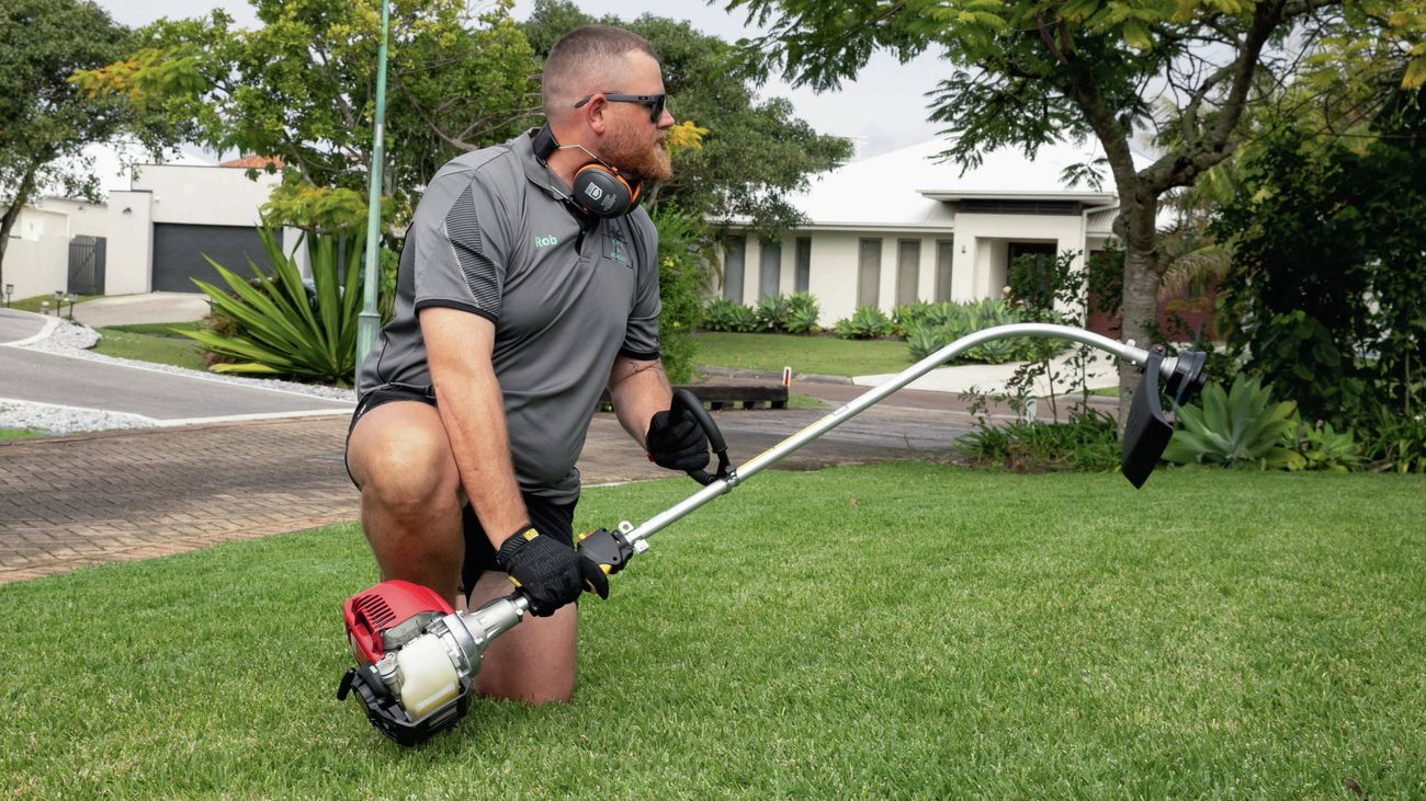 Person mowing grass in a residential yard with warm sunlight in the background.