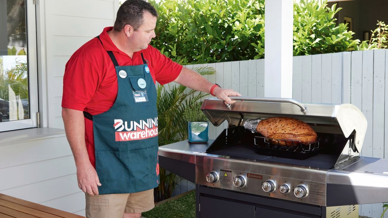 A Bunnings employee closes the hood of a BBQ with ham inside.