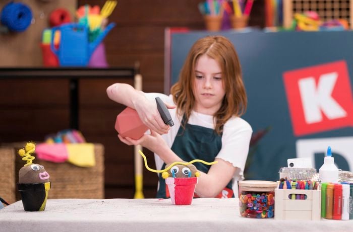A young girl is watering a decorated grass head placed in a pot at a Bunnings DIY workshop.