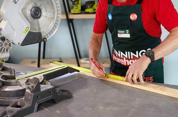 A person marking length on a timber panel using a measuring tape and pencil