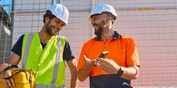 Two tradesman on a jobsite wearing PPE with a phone.