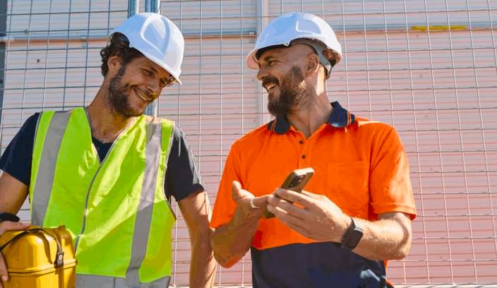 Two tradesman on a jobsite wearing PPE with a phone.
