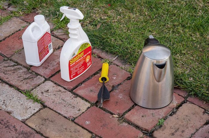 Weed removal products, weeder tool and kettle outside on a footpath.