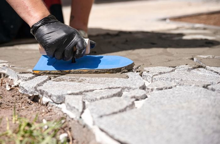 Applying grout in between each paver at an angle.