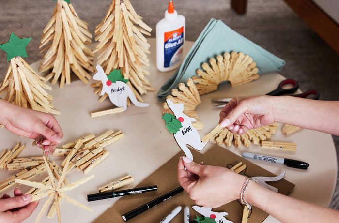 Two people crafting Christmas decorations on a table, featuring clothes peg trees, kangaroo-shaped place holders, glue and markers.