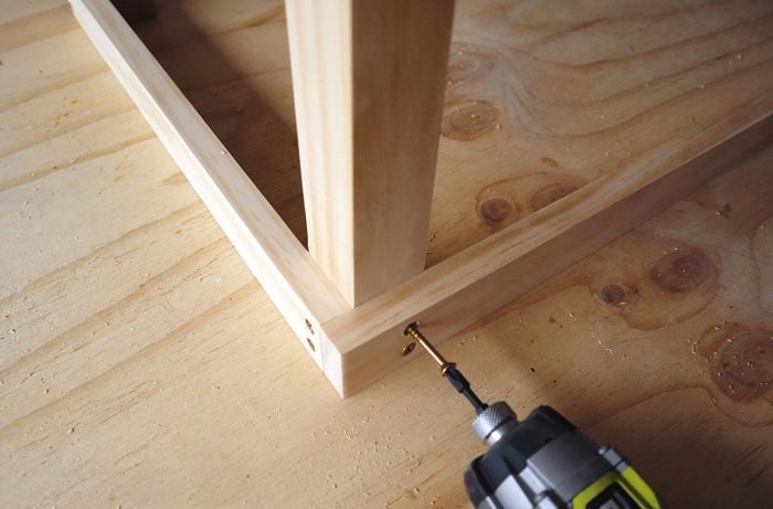 Person drilling screw connecting timber frame to legs