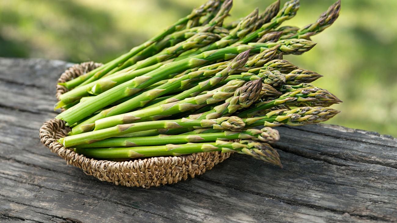 A woven bowl of freshly picked asparagus on a wooden outdoor table