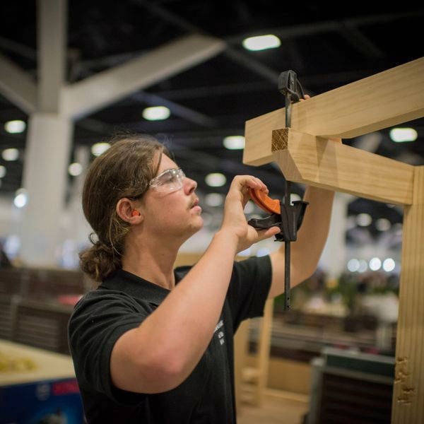 A person using a clamp to secure timber while working on a wooden frame in an indoor workshop setting
