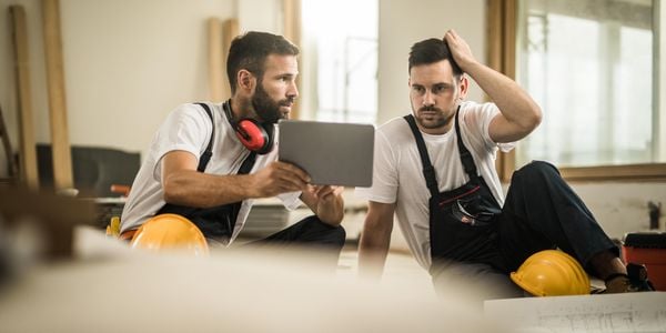 A construction worker showing a colleague something thought provoking on his laptop on a building site