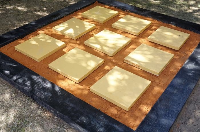Nine pavers laid out in a square on a bed of sand with a border of sleepers