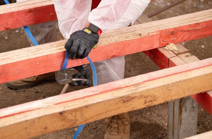 The image shows a person in protective gear is installing a support strapping beneath the joists to hold the insulation batts in place. 