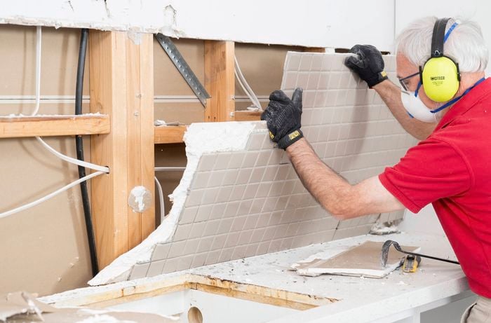 A Bunnings Team Member is removing a splashback from a kitchen wall. 
