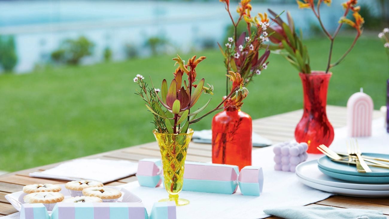 Blue and purple crackers sit on an outdoor table amongst red and yellow glass vases.