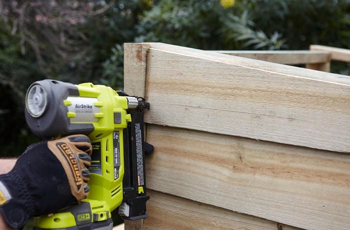 A timber plank being nailed to the side of a chicken coop by a Bunnings team member with a nail gun