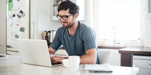 Smiling man using laptop on kitchen bench