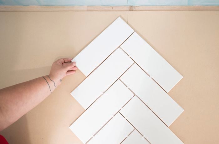 A person is dry laying white rectangular tiles in a herringbone pattern on a flat surface.