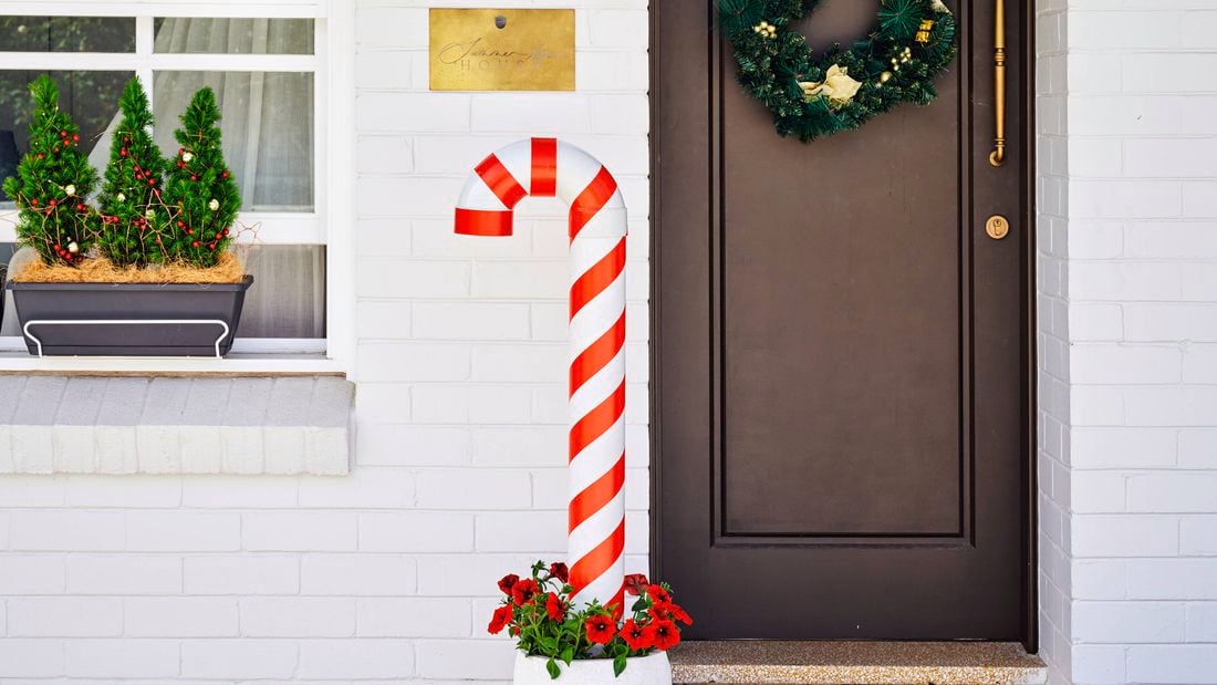 A wide shot of a front door of a house with a giant Christmas candy cane at the right on the porch.