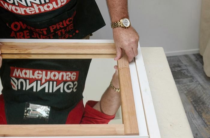 A person fixing a timber frame around the edge of a mirror
