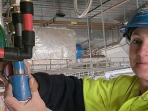 : A female plumber wearing yellow hi-vis and a blue helmet while fitting REHAU pipes.