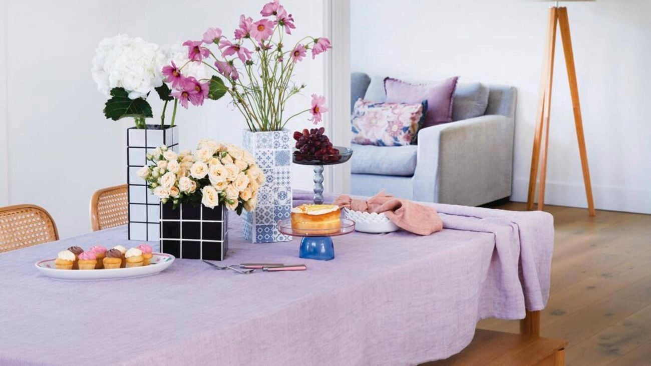 Wooden table with a purple tablecloth, covered with tiled flower boxes, fresh flowers and cupcakes