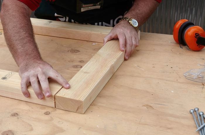 A person positioning lengths of pine timber to make a frame