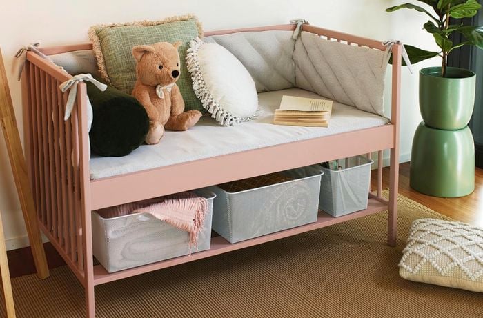 Completed light pink reading nook carrying grey pillows and an open book. 2 Grey mesh storage containers carry a blanket and books underneath the seats