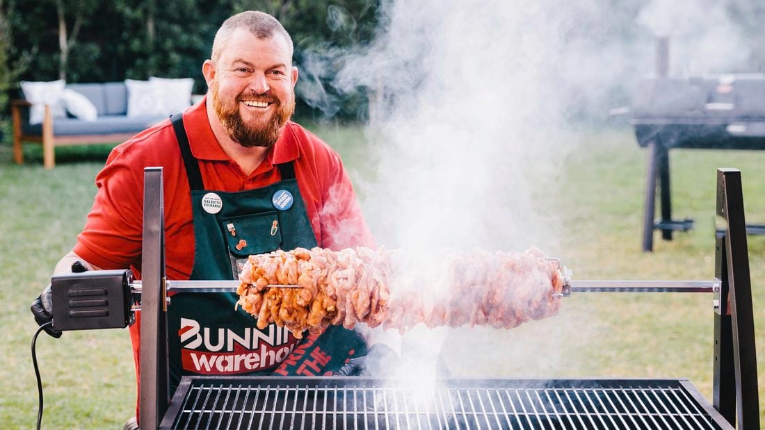 Man standing next to a spit roaster with meat on a rotisserie