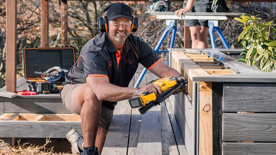 A tradesperson wearing safety glasses and using a DeWALT nail framer on an outdoor deck.