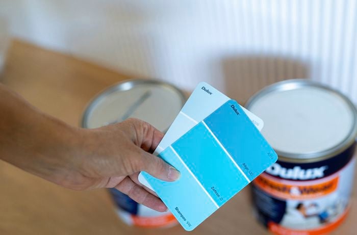 A person is holding blue paint colour swatches to help choose the right shades for a colour capping wall painting project. 