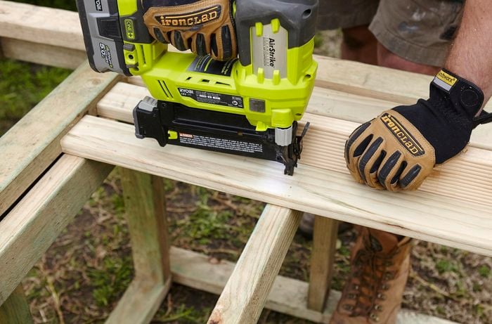 Wooden slats being nailed into place as a raised floor for a chicken coop with a nail gun, using a piece of scrap timber as a base