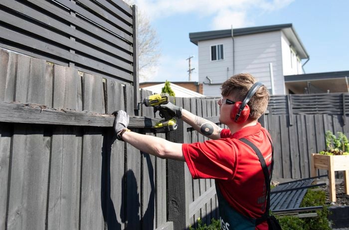 Bunnings team member drilling a fence extension into a wooden fence wearing safety ear muffs, glasses and gloves