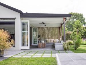 A patio space that opens from french doors, featuring geometric brick pavers on grass.