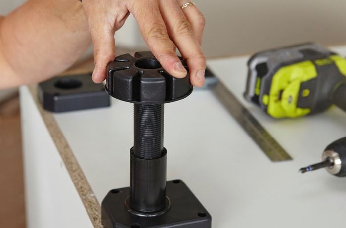 Person screwing cabinet feet into foot plate