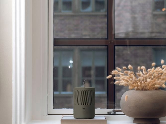 Stylish grey moisture absorber sitting on a window sill next to a vase