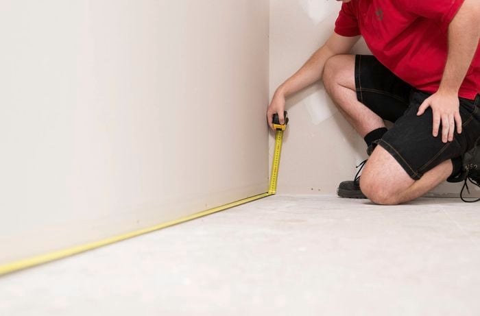 A Bunnings Team Member is measuring the length and width using a measuring tape to measure the area.