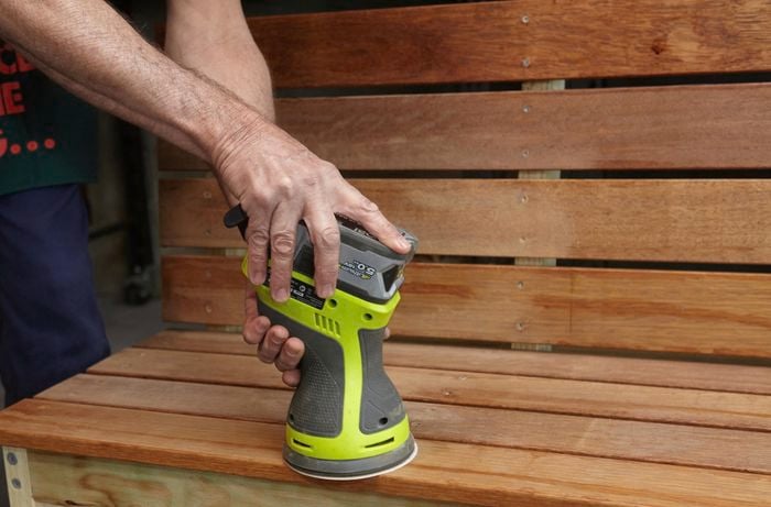 Person machine sanding wooden DIY garden bench.