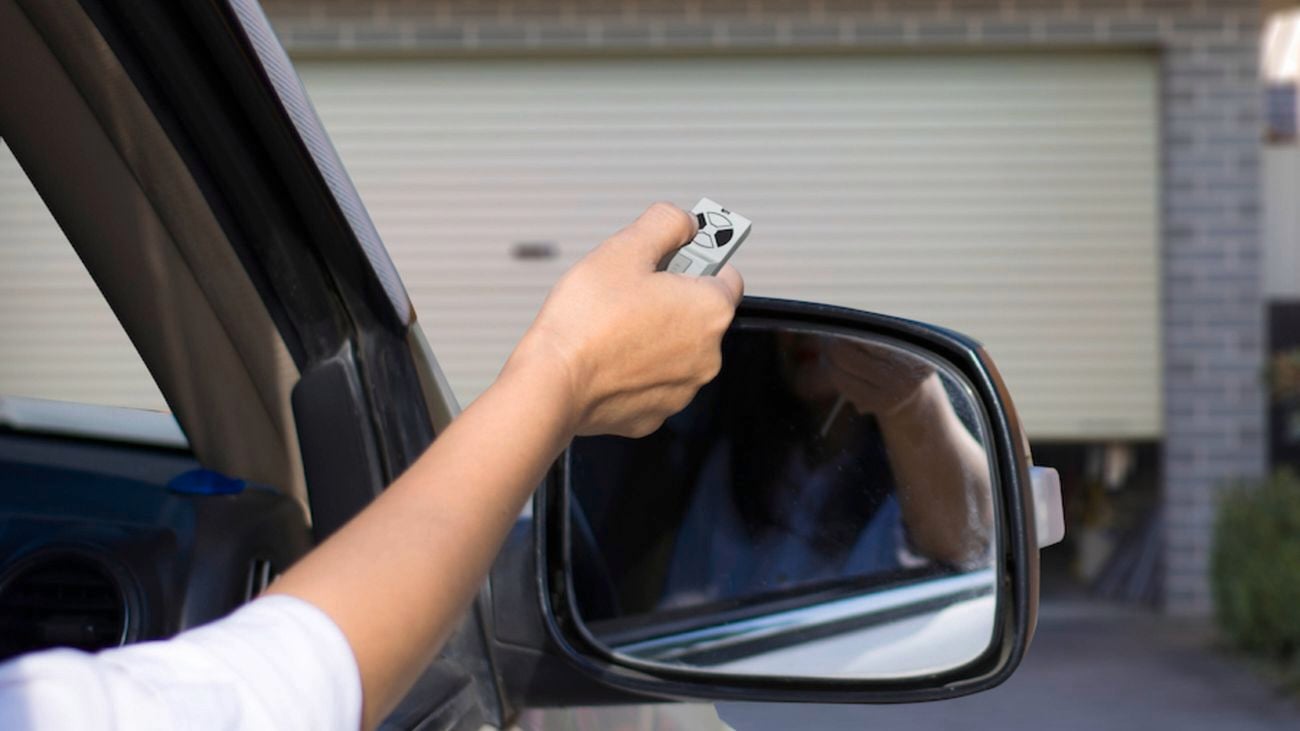 Hand out car window holding remote in front of garage door.
