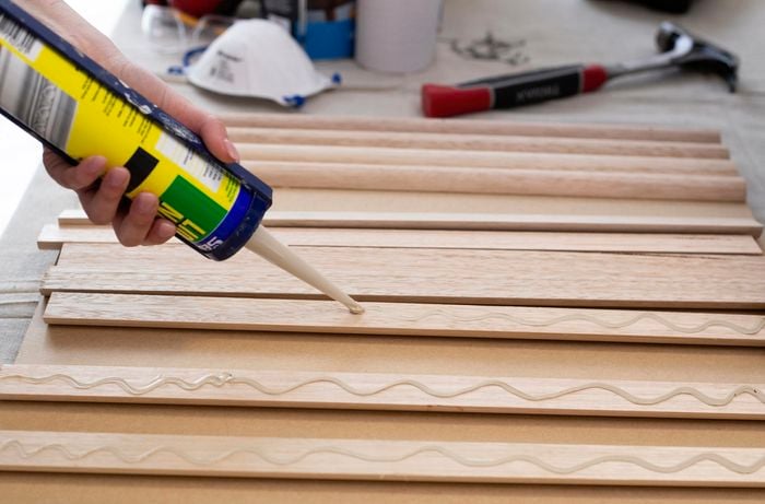 Person using liquid nails on back of timber dowels.