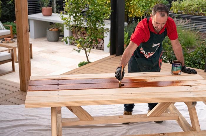 Using a paintbrush to stain the wooden picnic table