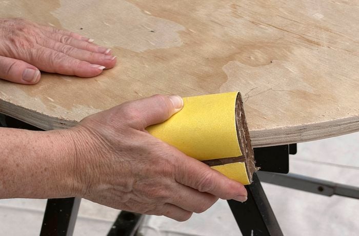  A close up image of a hand using a sanding block with yellow sand paper to sand the edge of a circular piece of timber.