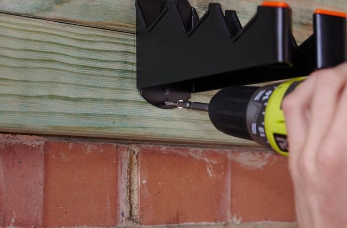 A person attaching a hanger to a timber beam on a garage wall using a cordless drill