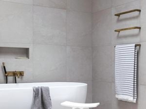 Freestanding bath with foliage in the background and grey bathroom tiles
