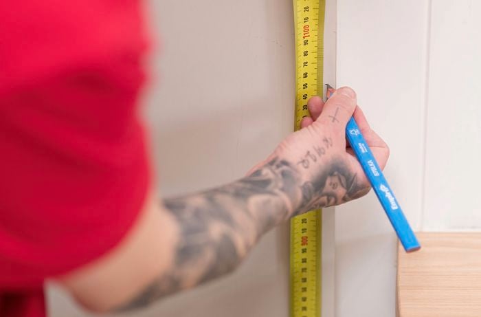 Mark measurements on a wall to measure the standard door handle height 